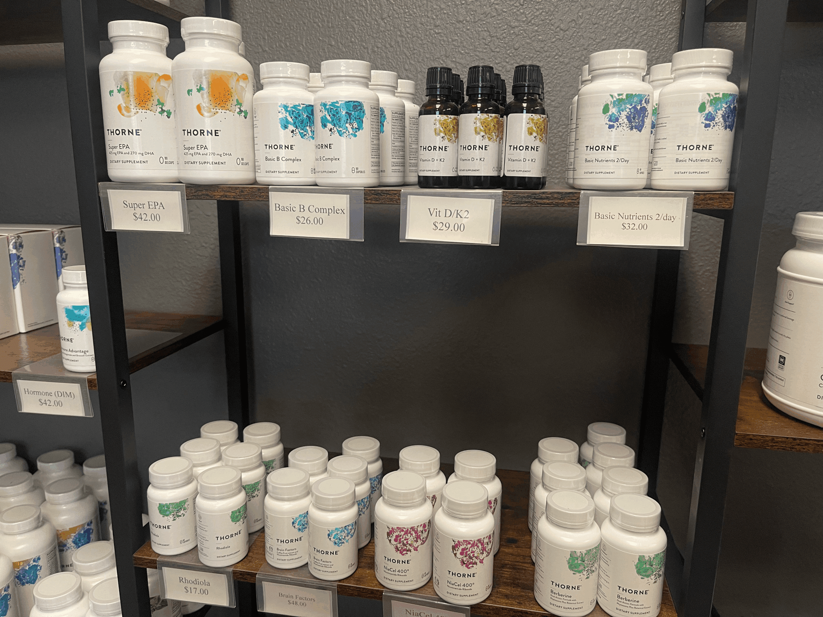 5928a6_65c1d276ba6f4daba11c8d58318a73e4~mv2 shelf displaying various Thorne dietary supplements and nutraceuticals including Super EPA, Basic B Complex, Vitamin D/K2, Basic Nutrients 2/day, Rhodiola, Brain Factors, NiaCel 400, and Berberine with price tags in a wellness clinic setting promoting premium supplement support for hormone optimization, weight loss, and overall healthspan management